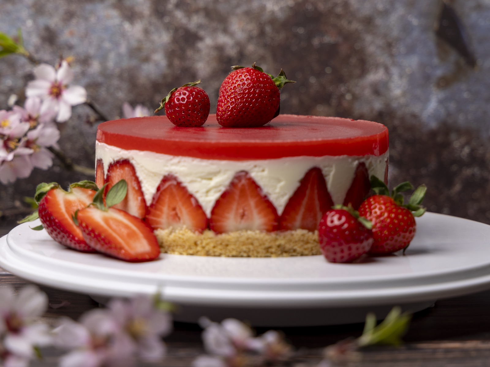 Ein rundes, geschichtetes Dessert steht auf einem weißen Teller und besteht aus einer roten Geleeschicht oben, einer weißen Cremeschicht in der Mitte und ein…