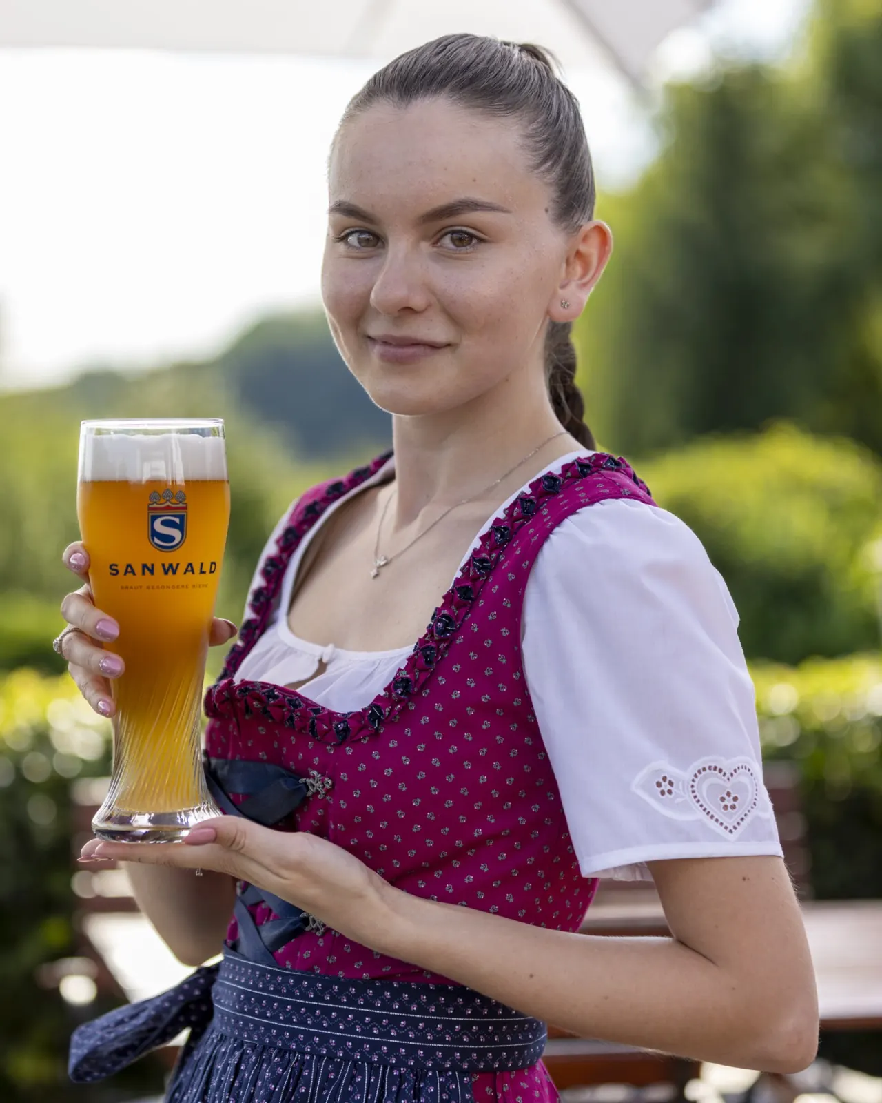 Frau im Dirndl serviert ein Weizenbier im Biergarten